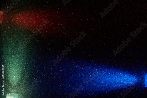 On a dark background in a multi-colored fine grain, rays of red turquoise and blue light