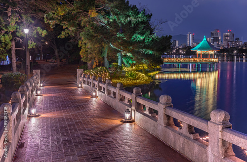 fukuoka, kyushu - december 06 2021: Stone Kangetsu bridge created in march 1927 lighted-up with luminous glass lanterns crossing the pond of Ohori Park and leading to the illuminated Ukimi-do Pavilion