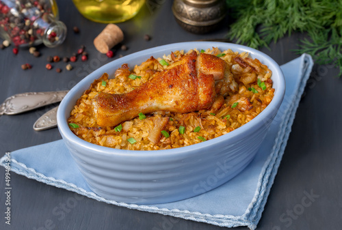 Chicken Bulgur pilaf. Roast chicken drumsticks and bulgur wheat in individual casserole. Horizontal, selective focus, dark background.