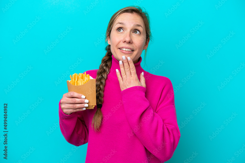 Young caucasian woman holding fried chips isolated on blue background looking up while smiling Young caucasian woman holding fried chips isolated on blue background looking up while smiling