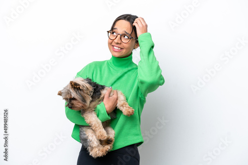 Young hispanic woman holding a dog isolated on white background having doubts and with confuse face expression