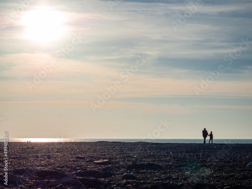 Father and son on a spring pebble beach at sunset. Silhouettes of people on the shore. Vacation on the beach. Rest on the sea. Rocky shore.
