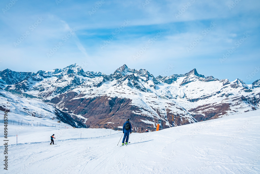 Skiers skiing on snow covered slope against mountain range during winter Skiers skiing on snow covered slope against mountain range during winter