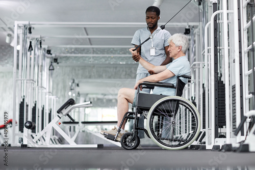 Side view portrait of senior man in wheelchair doing exercises in gym at healthcare clinic, copy space