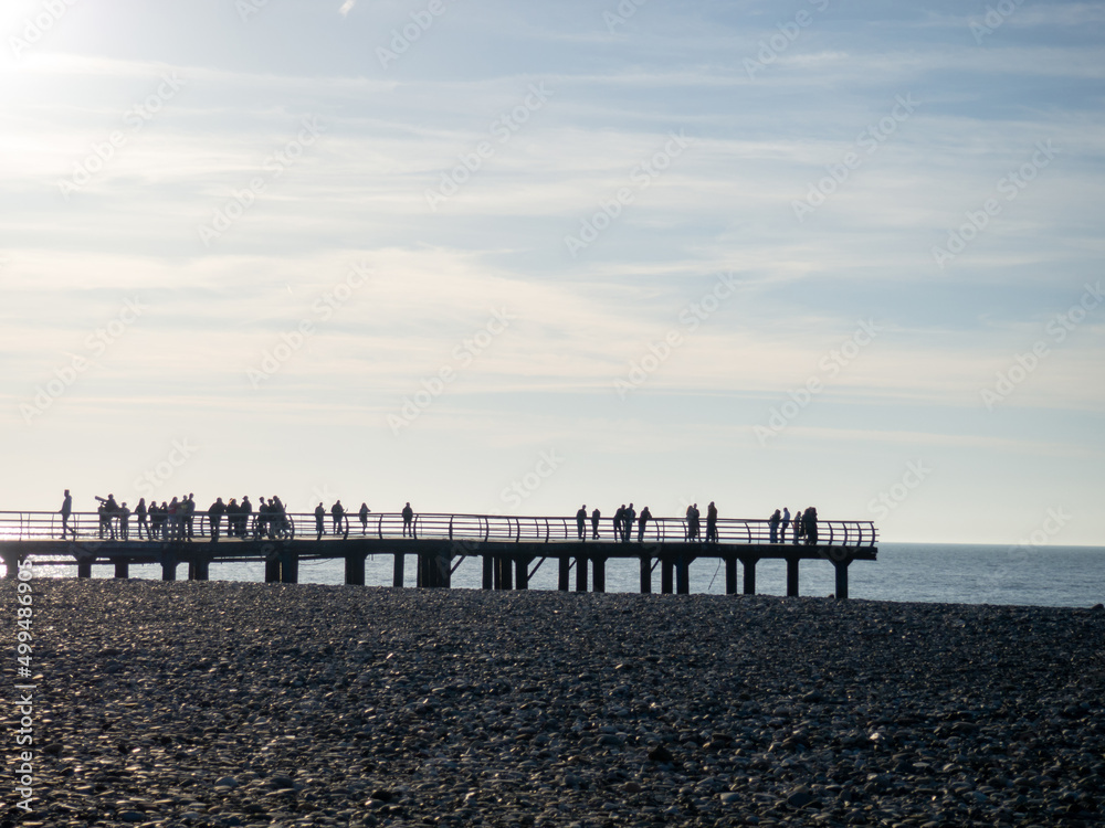 Obraz premium Silhouettes of people on the bridge on the seashore. People see off the sunset. Sea coast. Pier on the sea.