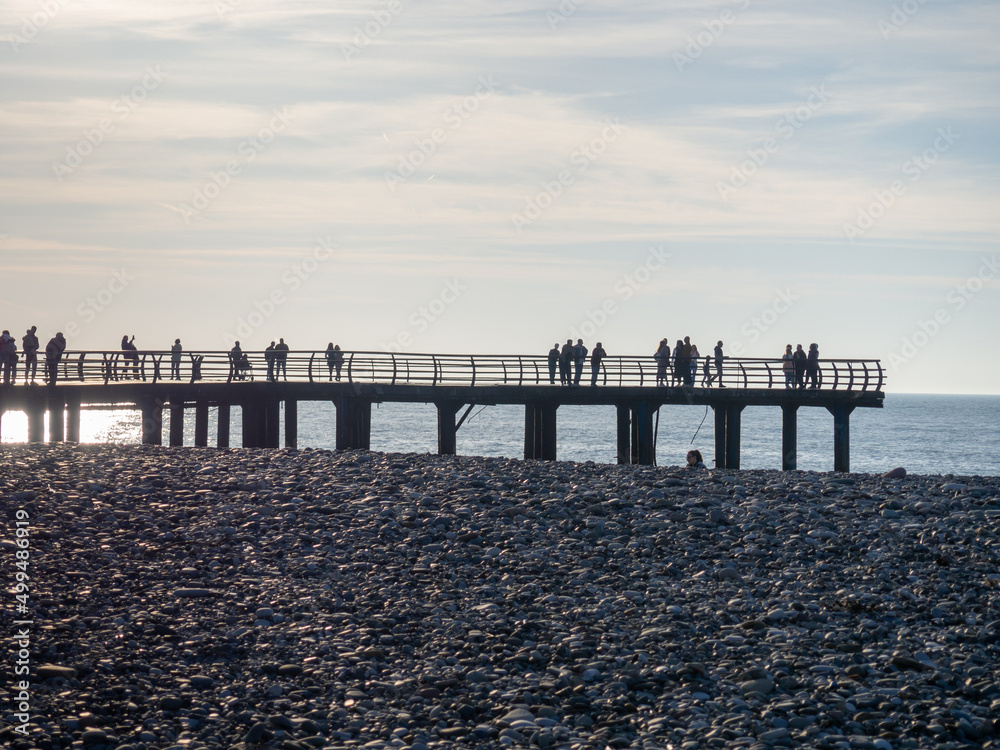 Obraz premium Silhouettes of people on the bridge on the seashore. People see off the sunset. Sea coast. Pier on the sea.