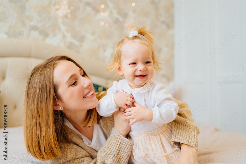 Cute mom and baby daughter lie down, play and hug in bed. games with children. Cute mom and baby daughter lie down, play and hug in bed. games with children.