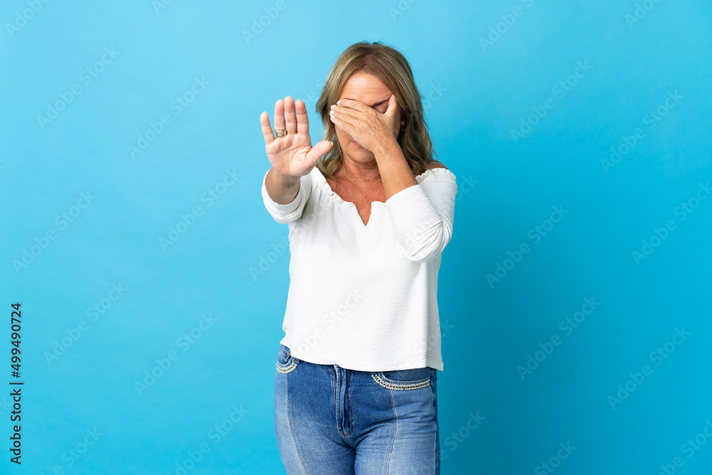 Middle aged blonde woman over isolated background making stop gesture and covering face Middle aged blonde woman over isolated background making stop gesture and covering face
