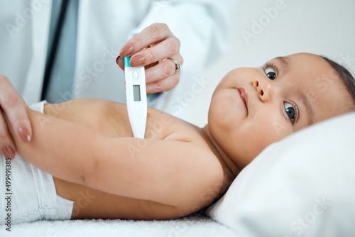 Lets start by taking your temperature. Shot of a paediatrician taking a babys temperature with a thermometer in a clinic.
