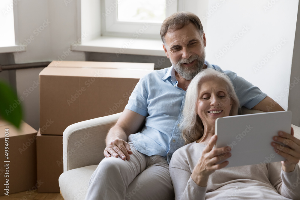 Older couple relax on sofa on move day near boxes with stuff, use tablet buy goods on internet, make order via e-service app, make purchase online, search home renovation new ideas, e-commerce concept Older couple relax on sofa on move day near boxes with stuff, use tablet buy goods on internet, make order via e-service app, make purchase online, search home renovation new ideas, e-commerce concept