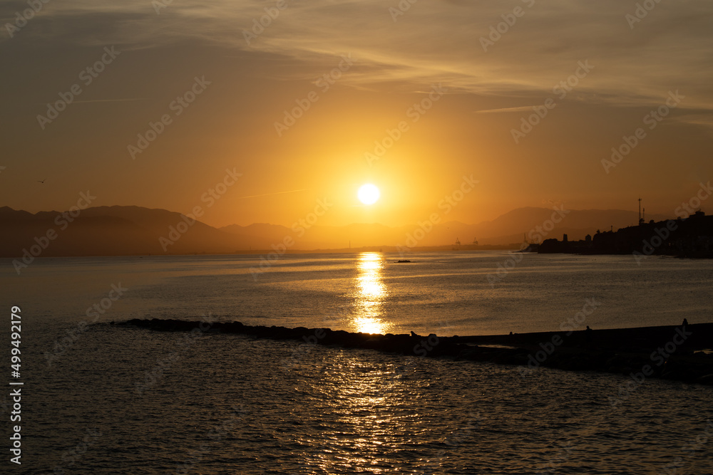 puesta de sol de un cielo anaranjado con un embarcadero que sale de la playa 