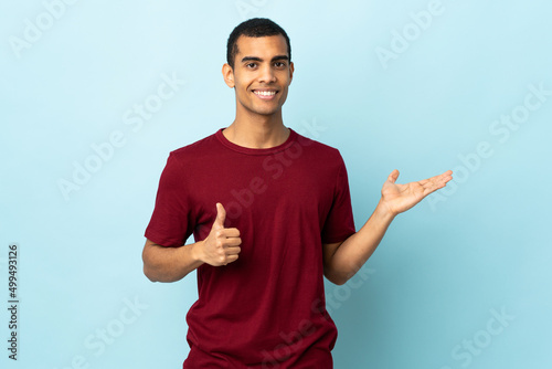 African American man over isolated background holding copyspace imaginary on the palm to insert an ad and with thumbs up