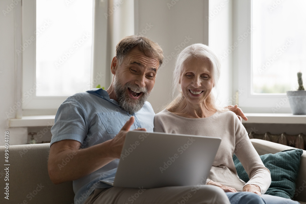 Smiling elderly couple watch movie funny videos look overjoyed, read  fantastic news feels excited staring at laptop screen relax on sofa at home.  Celebrate online lottery, giveaway win success concept Stock Photo |