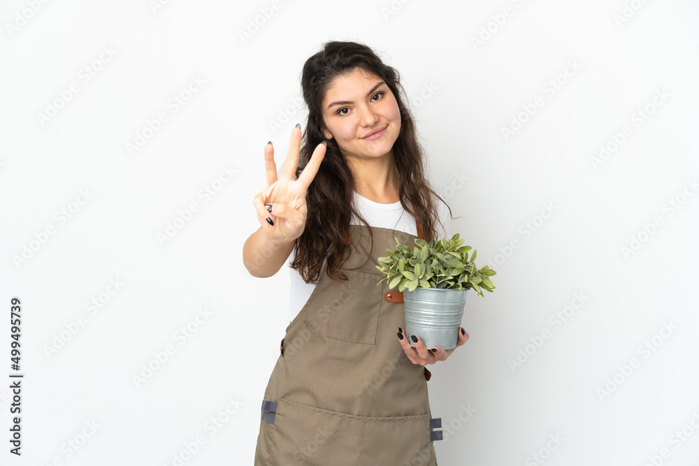 Young Russian gardener girl holding a plant isolated happy and counting three with fingers
