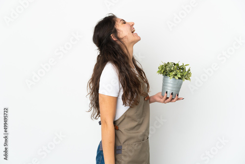 Young Russian gardener girl holding a plant isolated laughing in lateral position