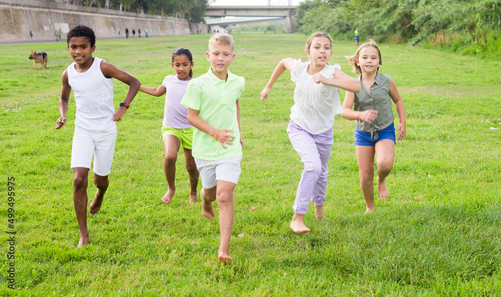 Multi-ethnic group of school children laughing and running in a city park at summer day