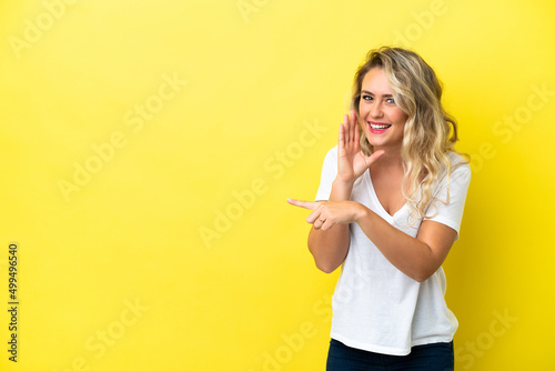 Young Brazilian woman isolated on yellow background pointing to the side to present a product and whispering something