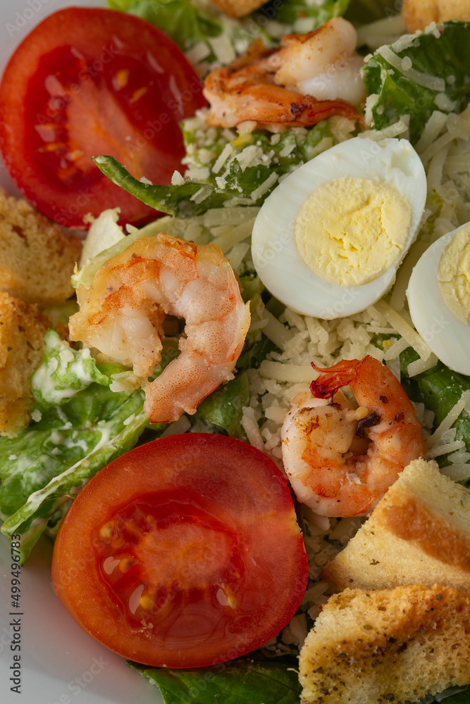 Caesar salad with grilled shrimps, tomato, boiled egg, lettuce, croutons and green sauce. Top view close-up on a brown round plate with fresh vegetables and cutlery by side on a dark background. Caesar salad with grilled shrimps, tomato, boiled egg, lettuce, croutons and green sauce. Top view close-up on a brown round plate with fresh vegetables and cutlery by side on a dark background.