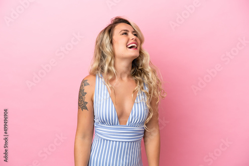 Young Brazilian woman in swimsuit in summer holidays isolated on pink background laughing