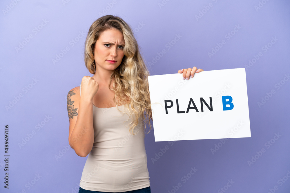 Young Brazilian woman isolated on purple background holding a placard with the message PLAN B and angry Young Brazilian woman isolated on purple background holding a placard with the message PLAN B and angry