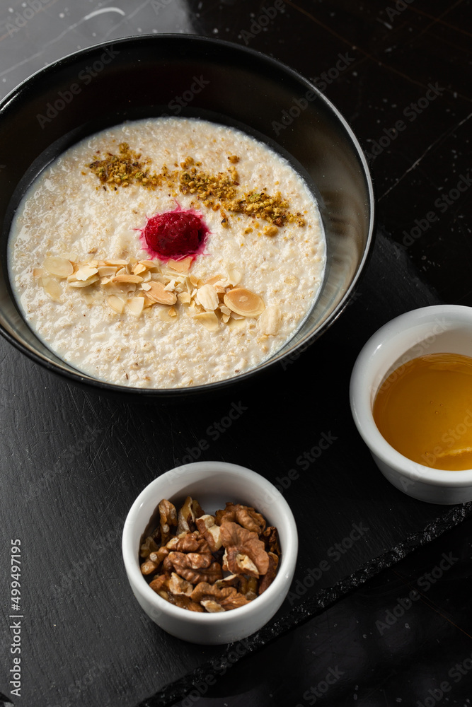 Semolina porridge for breakfast oat with nuts in black bowl served with honey isolated on black stone background. Homemade food. Tasty breakfast. Selective focus.