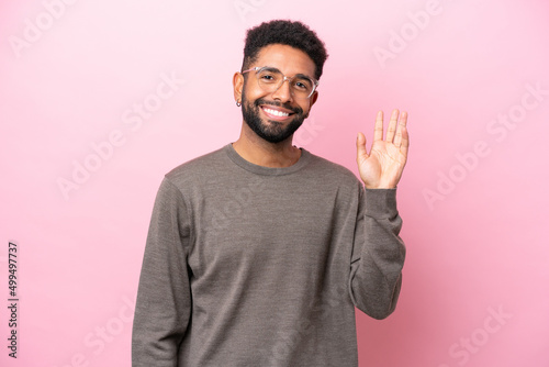 Young Brazilian man isolated on pink background saluting with hand with happy expression