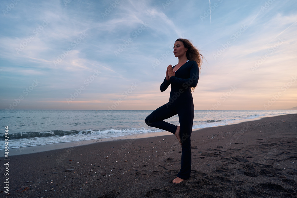 woman doing a yoga practice at the beach while a beautiful sunset