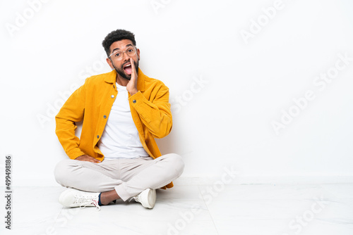 Young Brazilian man sitting on the floor isolated on white background shouting with mouth wide open