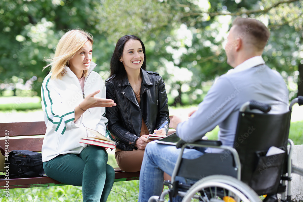 Two women and a man in wheelchair communicate in park Two women and a man in wheelchair communicate in park