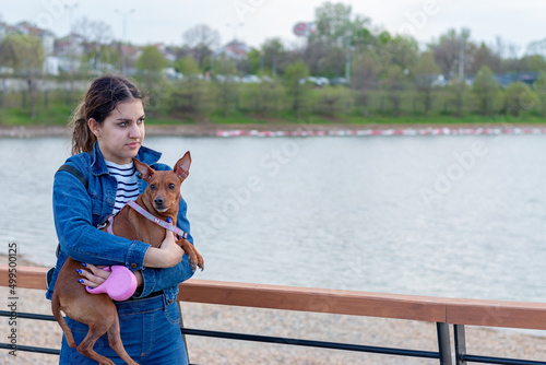A teenage girl holding  a miniature pincher in her arms by the lake.Concept of relationship between human and animal.