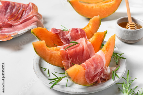 Prosciutto ham with melon cantaloupe slices, honey and rosemary in a plate on white background. Italian appetizer
