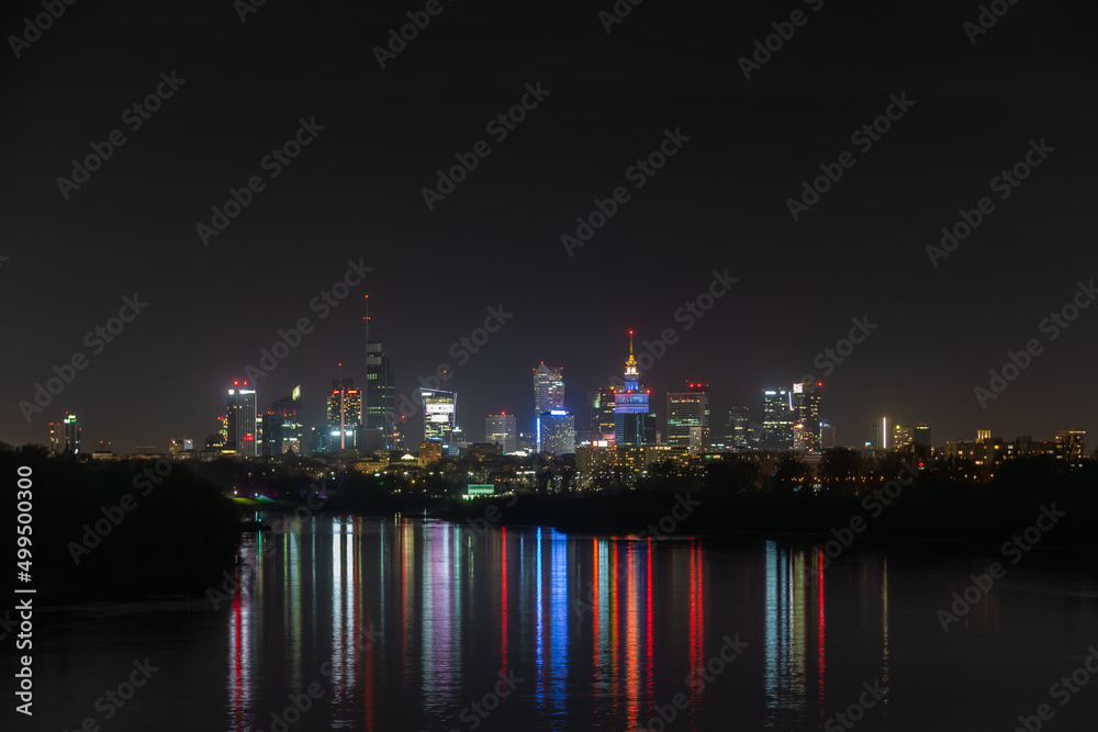 Obraz premium Night in big city of Warsaw skyline, high skyscrapers illumination reflected on Wisla river surface. Downtown beautiful cityscape panorama. Capital of Poland