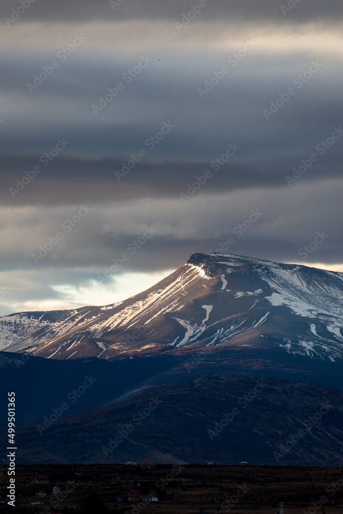 colina y montañas con nieve, con nubes grises de lluvia y nieve, rayo de sol en atardecer