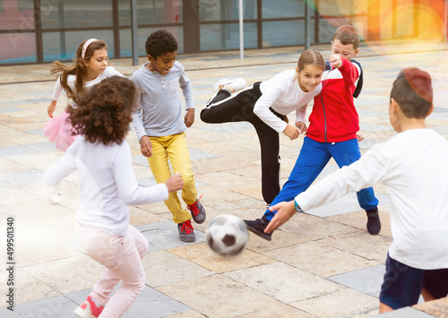 Cuadro en lienzo Happy tween girls and boys of different nationalities playing football in schoolyard during break in lessons on warm fall day