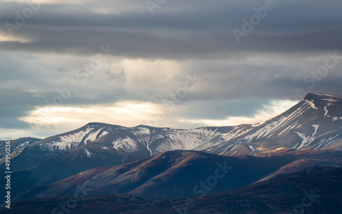 colina y montañas con nieve, con nubes grises de lluvia y nieve, rayo de sol en atardecer