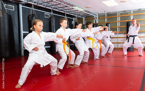 Group of preteen boys and girls doing karate kicks with male coach during karate class