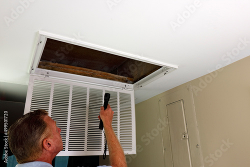 Adult Man Shining Flashlight Into HVAC Intake Vent in a Home Entry.