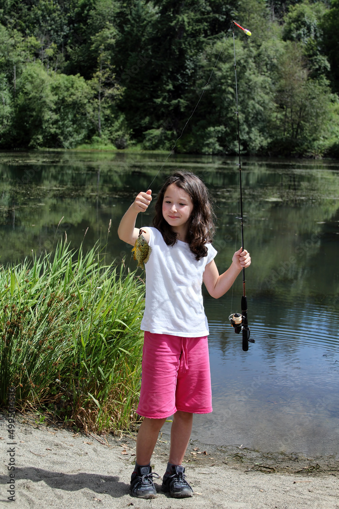 Young girl admiring her sunfish she caught while fishing in a small pond Young girl admiring her sunfish she caught while fishing in a small pond