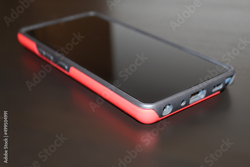 mobile phone with red protective case with blank screen on black table