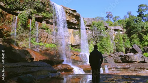 young man enjoying the pristine natural waterfall falling from mountain top at day from low angle video taken at phe phe fall meghalaya india. photo