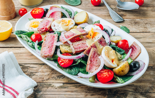 French Salad Nicoise with tuna steak, asparagus, tomatoes, eggs, potatoes and black olives on a white background.