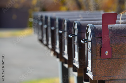 mailboxes in a row line up of multiple U.S. postal service black metal mail boxes in a row first mail box with red flag up signifying mail horizontal format fall background empty space for type 