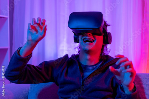 Man wearing virtual reality glasses is playing a 3D game with excitement, Bluetooth Remote Controller, VR, Future games, Gadgets, Technology, Red and blue background, VR game concept.