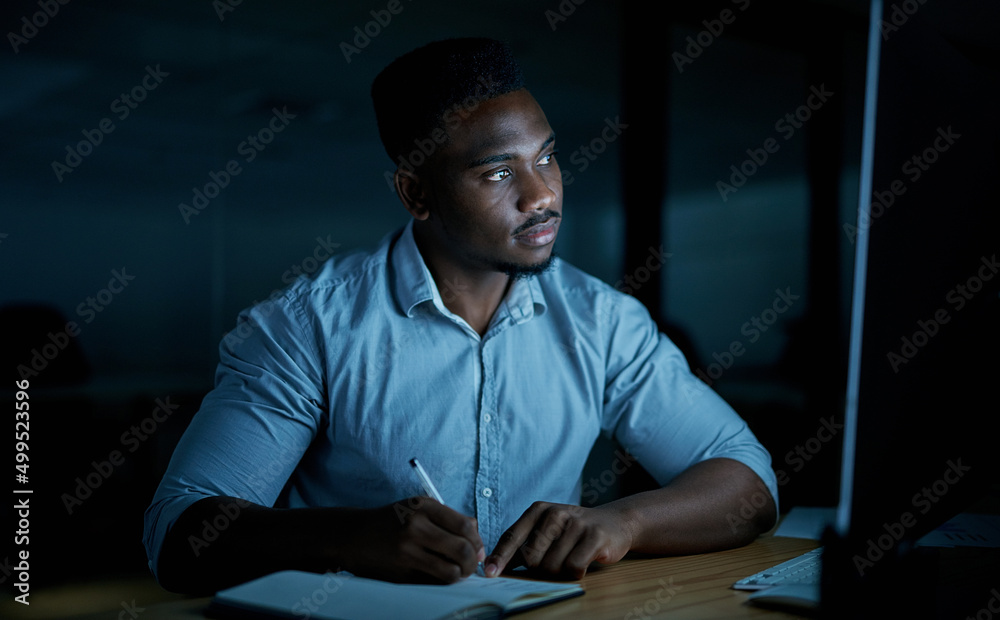 You cant finish a task without a bit of focus. Shot of a young businessman writing in a notebook and using a computer during a late night at work. - obrazy, fototapety, plakaty 
