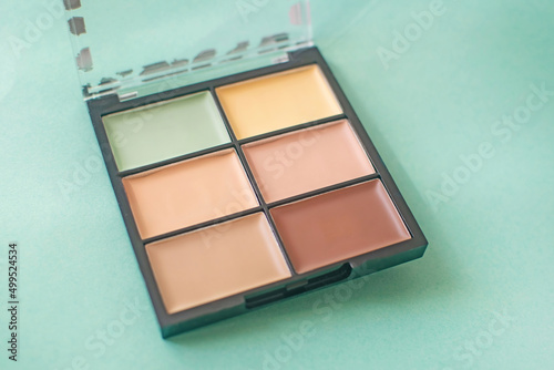 Make-up palette with colorful concealers on mint background.