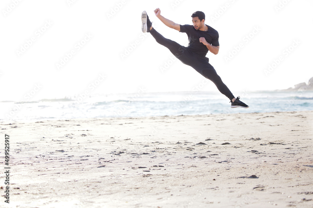 Kicking it into high gear. Full length shot of a handsome young male athlete working out on the beach. Kicking it into high gear. Full length shot of a handsome young male athlete working out on the beach.