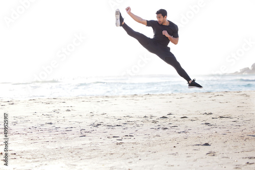 Kicking it into high gear. Full length shot of a handsome young male athlete working out on the beach.