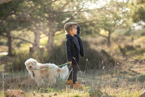 a little boy in vintage clothes walks in nature with a white shaggy dog in spring..