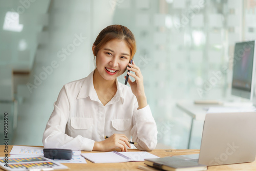 Successful Asian business woman smiling and talking on the phone at the office.