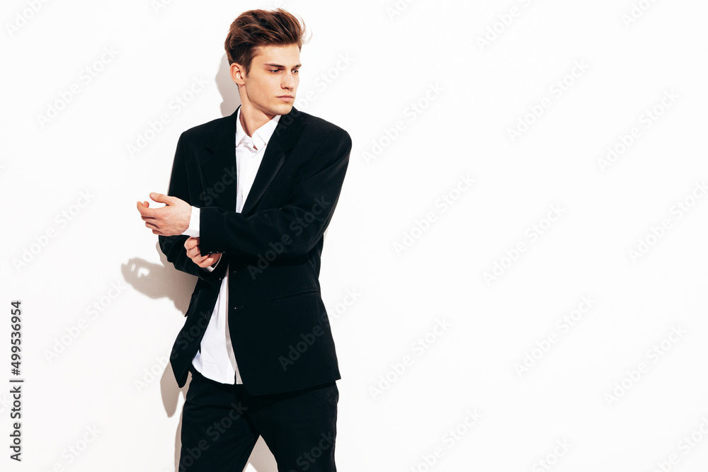 Portrait of handsome confident stylish hipster lambersexual model. Sexy modern man dressed in elegant black suit. Fashion male posing in studio near white wall. Isolated Portrait of handsome confident stylish hipster lambersexual model. Sexy modern man dressed in elegant black suit. Fashion male posing in studio near white wall. Isolated
